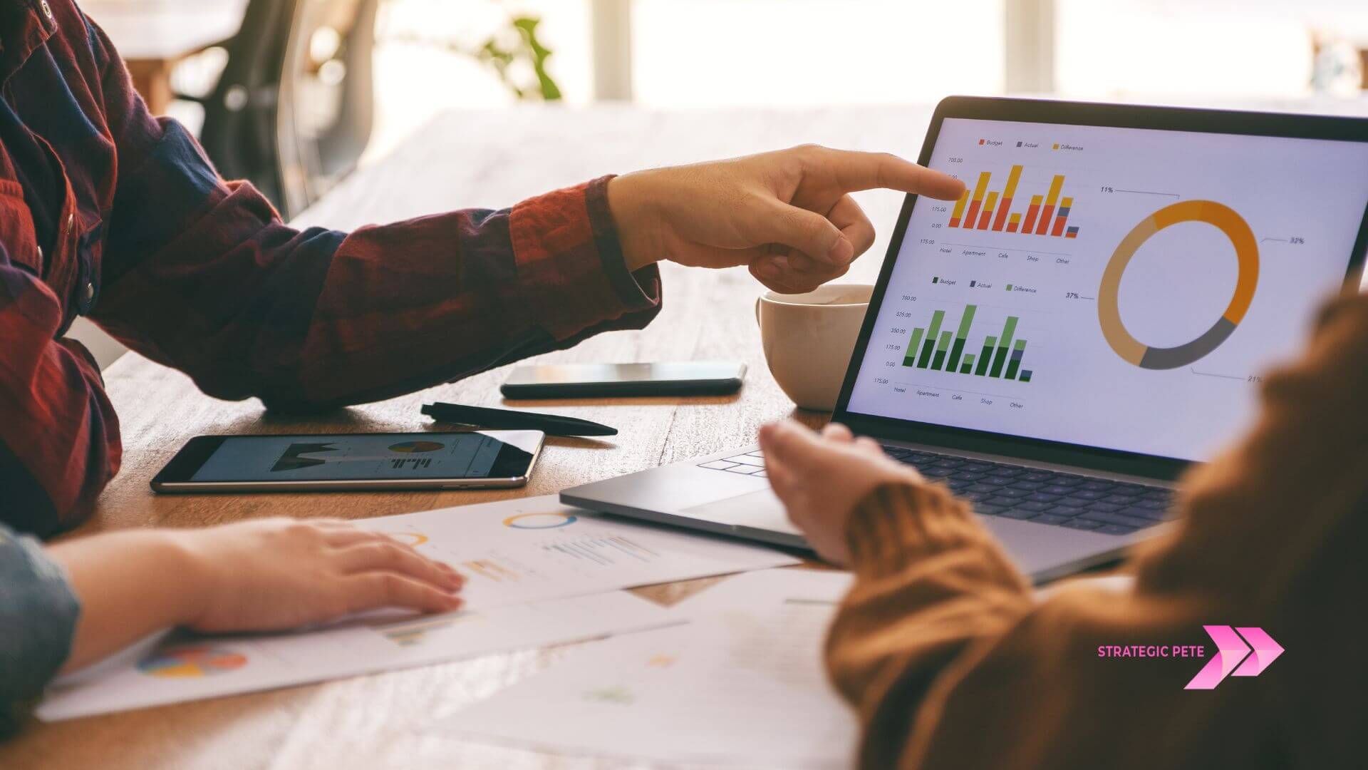Two people pointing at performance charts on a laptop and tablet at a desk