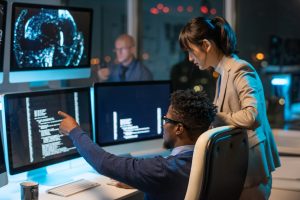 Two colleagues discuss AI marketing strategies, pointing at a large screen displaying data analytics in a corporate setting.