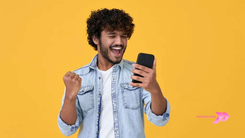 A man in a denim shirt celebrating while looking at his phone