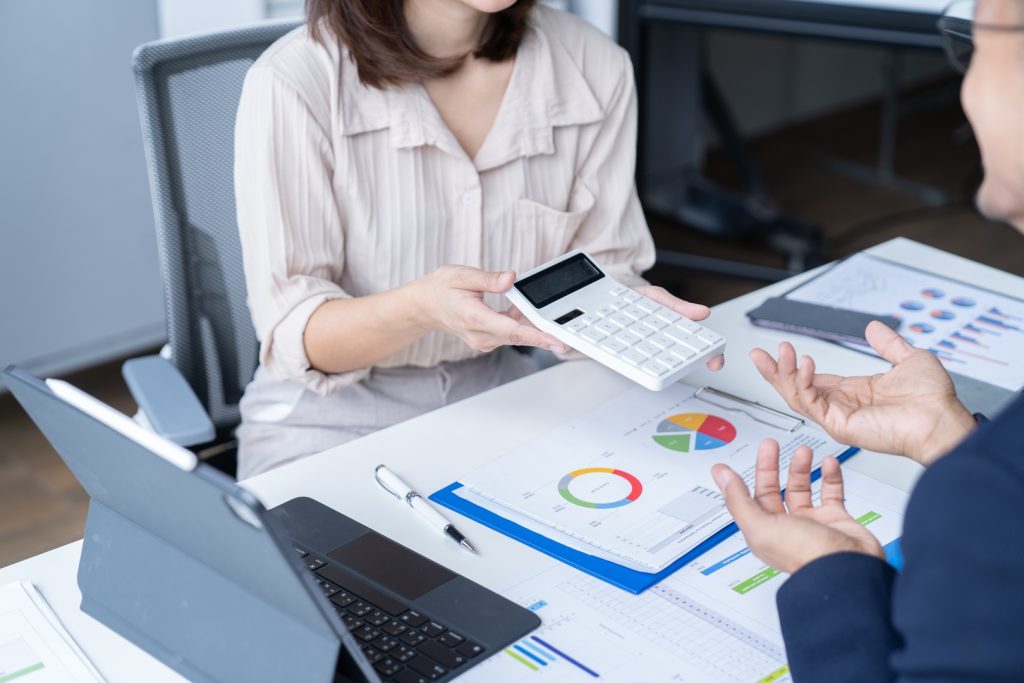 Two hands passing a calculator above data sheets, representing the decision-making process between strategy vs initiative in a business context.