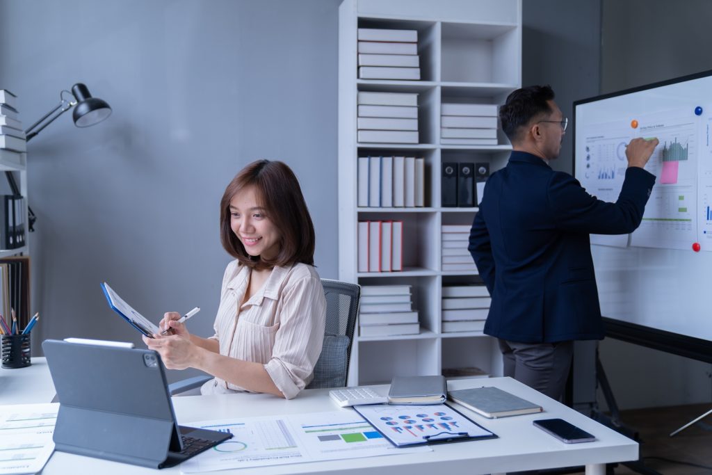 Two colleagues discussing marketing initiatives as one shows data on a tablet. One person points to the screen while the other listens attentively.