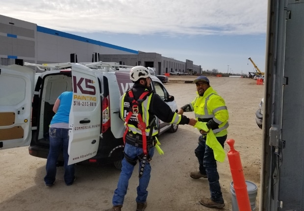 A work crew in high-visibility gear loading equipment beside a van on a job site