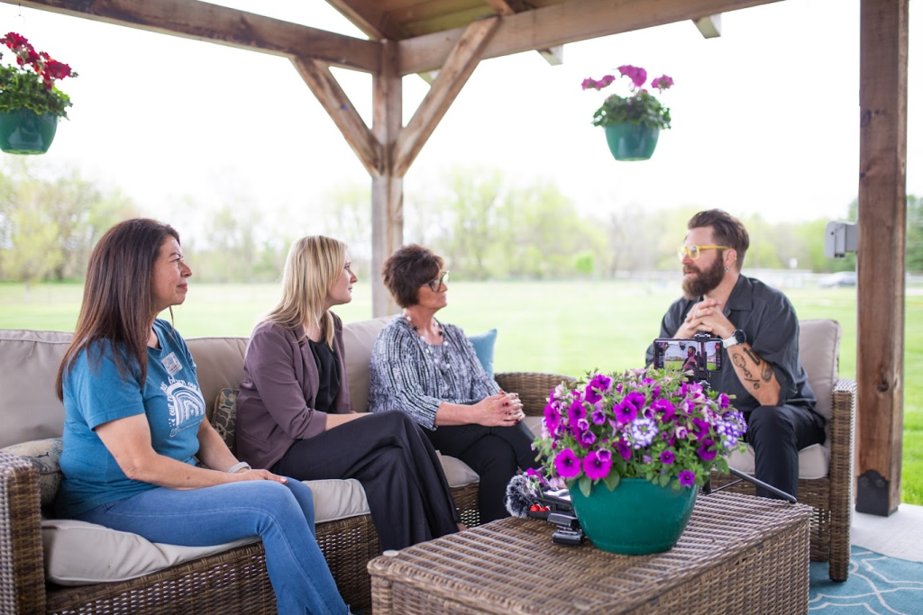 A film crew recording a conversation with residents and staff under an outdoor pergola