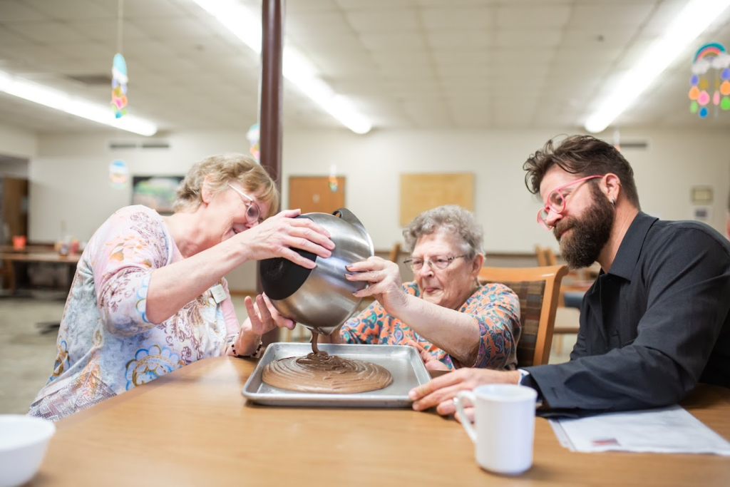 A resident and a staff member preparing food together while being filmed