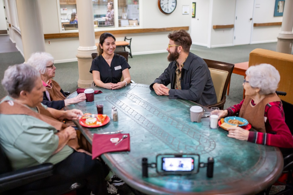Residents and staff around a table while a conversation is filmed