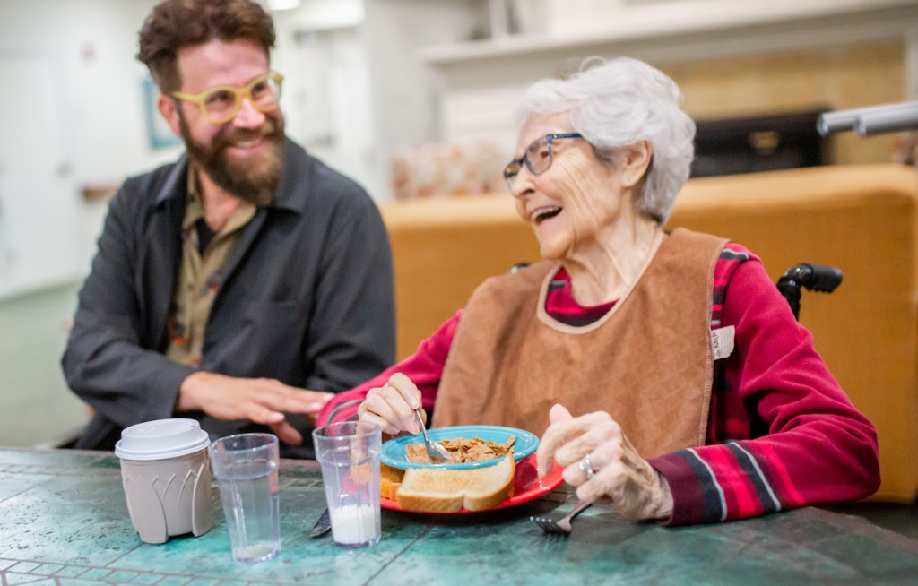 Peter Murphy Lewis sharing a laugh with an older woman at a care home table, filming People Worth Caring About