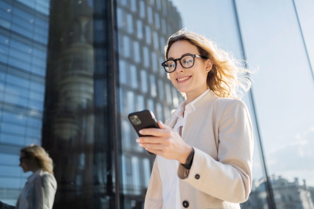 A businesswoman walking outside while using her phone, reflecting the role of a marketing expert in today’s digital world.