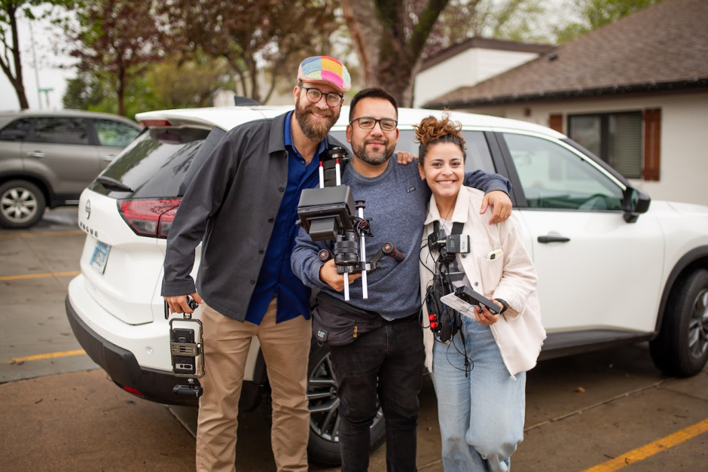 Film crew with camera equipment beside a car on location