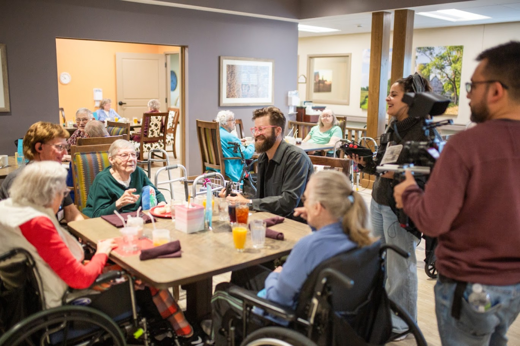 Residents and a film crew gathered in a care community lounge