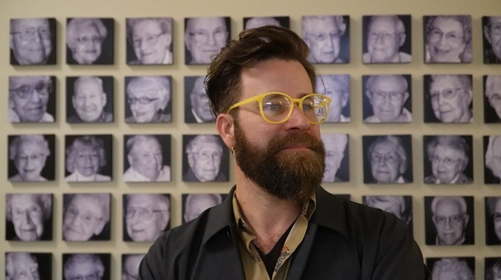 Peter Murphy Lewis being interviewed in front of a wall of resident portraits