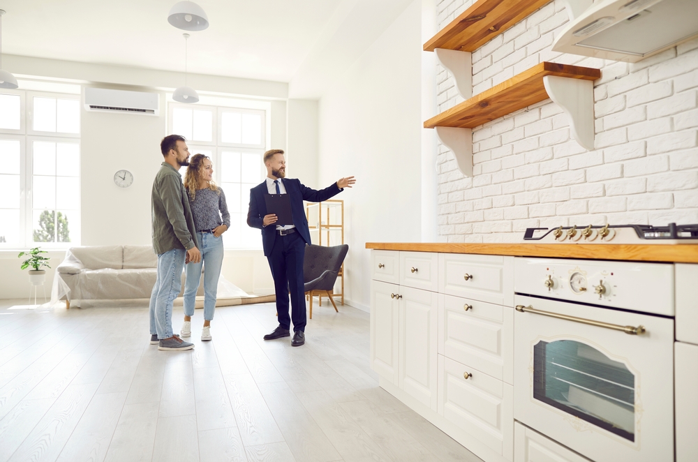A real estate agent showing a modern furnished apartment to a couple, illustrating the concept of executive rentals for business travelers and corporate tenants.