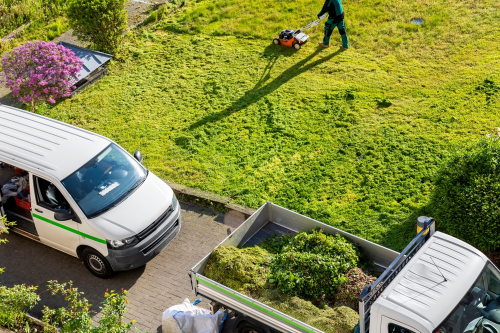 A landscaping crew mowing a lawn and loading green waste into trucks—an example of how to market a tree service business with clean branding, visible vehicles, and active field work.