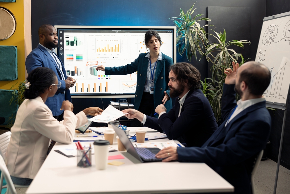 Team in a business meeting discussing charts and analytics on a large screen—illustrating strategies for how to market your business locally through data-driven decisions.