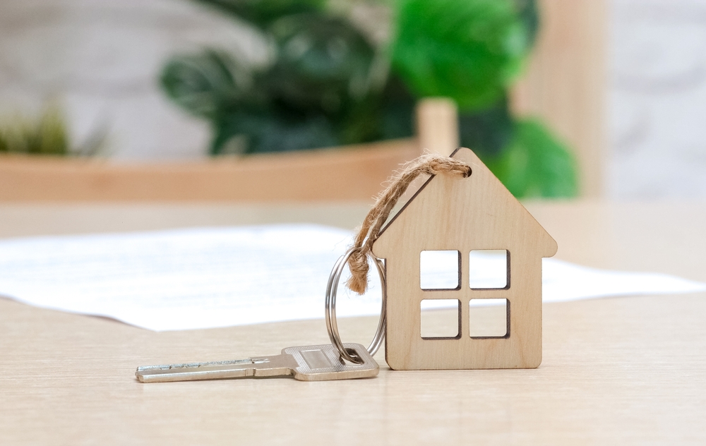 Close-up of a house-shaped keychain with keys on a table, symbolizing leases and corporate housing marketing for furnished rental properties.