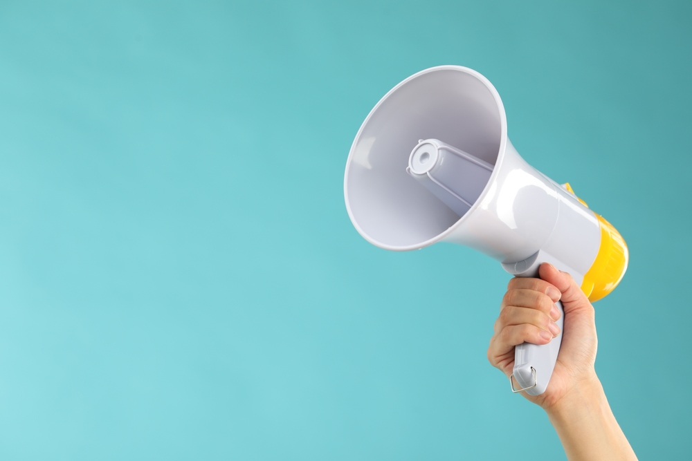 Hand holding a megaphone against a blue background, symbolizing local outreach and visibility—perfect for questions like how to promote your business locally.
