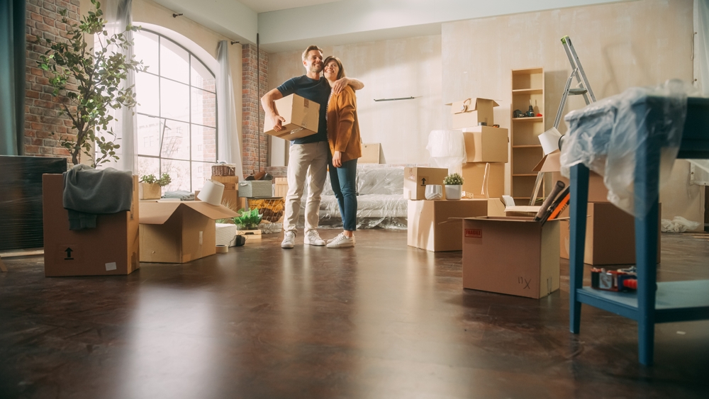 Couple standing in their new home surrounded by moving boxes and houseplants—an ideal visual for illustrating how to market a moving company through emotional storytelling and lifestyle imagery.