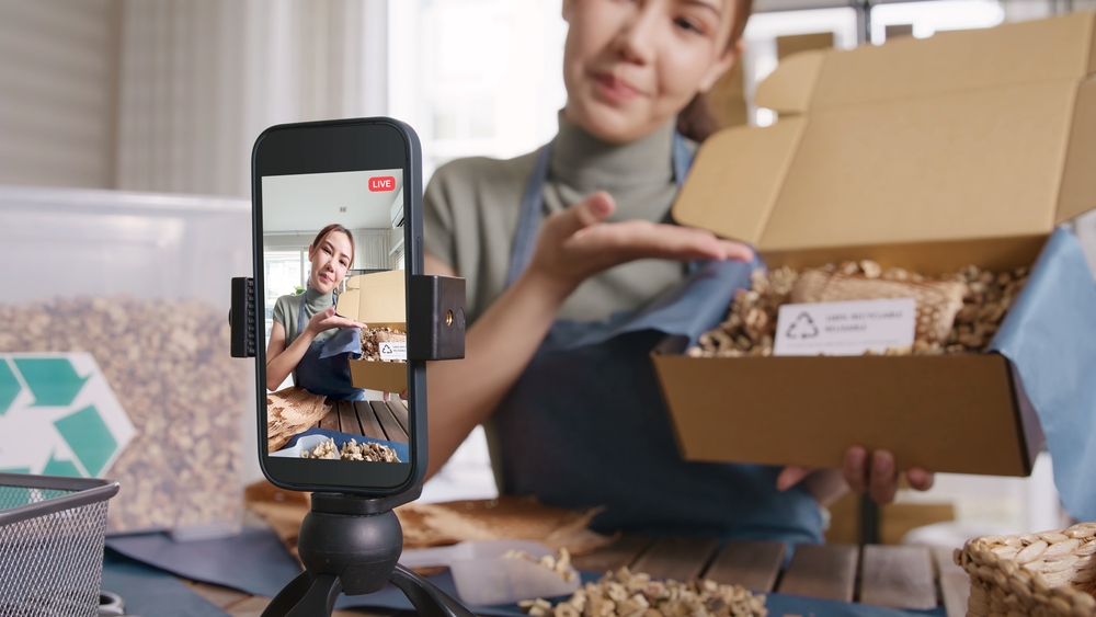 Young woman livestreaming unboxing of eco-friendly packaging materials on smartphone for social media; key strategy in Gen Z marketing.