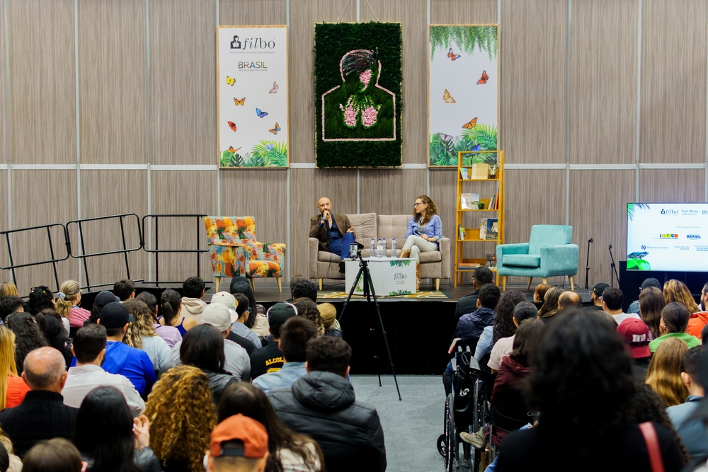 A packed audience listens to two speakers discuss strategies on stage at an international book fair, highlighting insights on how to promote your book through events, community, and reader engagement.