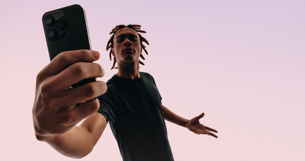 Young man with dreadlocks taking a selfie with a confident expression, holding a smartphone close to the camera, symbolizing marketing to Gen Z.
