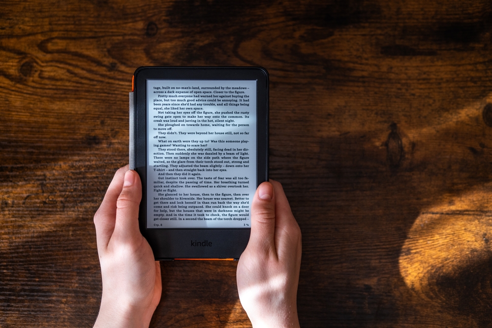 Hands holding an e-reader displaying a digital book on a wooden table, symbolizing modern publishing and creative book promotion ideas for authors in the digital age.