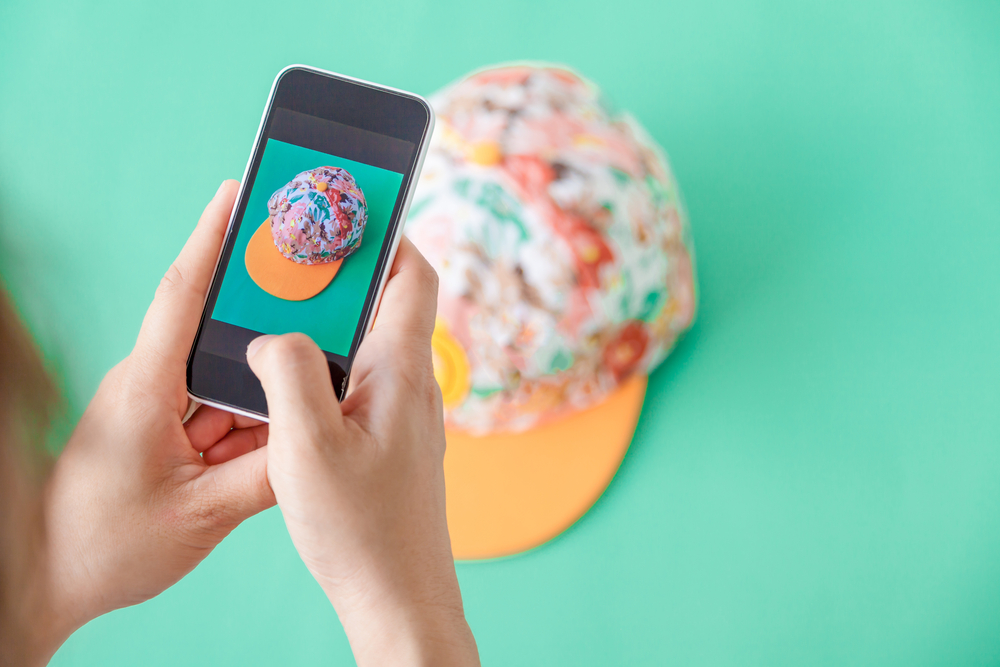 Close-up of person photographing a colorful, trendy cap with a smartphone against a vibrant background, a visual example of how to market to Gen Z through aesthetic content creation and social media engagement.