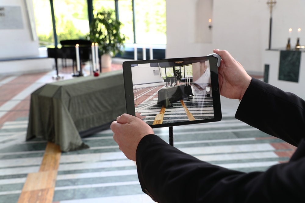 The image shows a person using a tablet to capture a funeral setting. This highlights how digital tools can enhance a funeral home marketing strategy. 