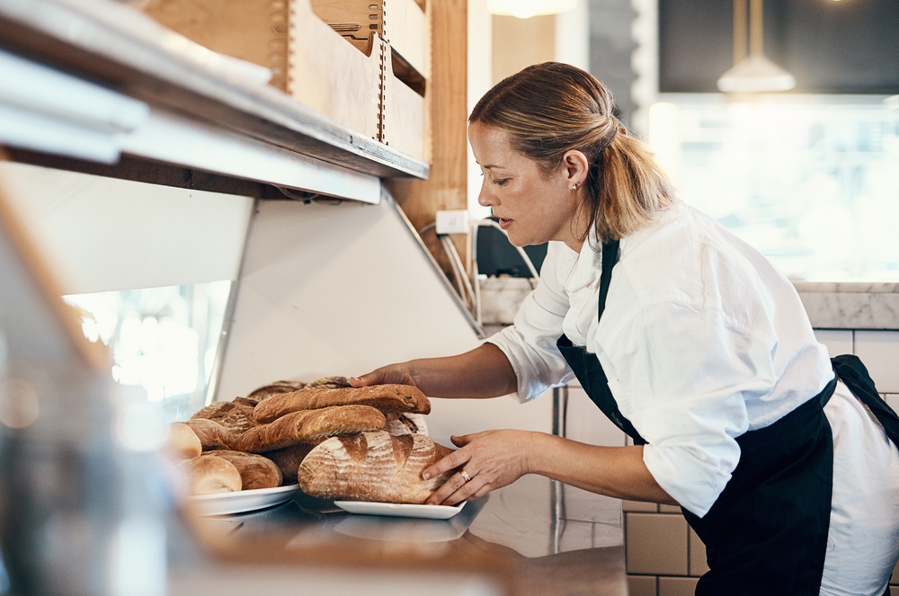 A bakery worker carefully arranging loaves of bread, illustrating how to market your restaurant by emphasizing quality in your products.