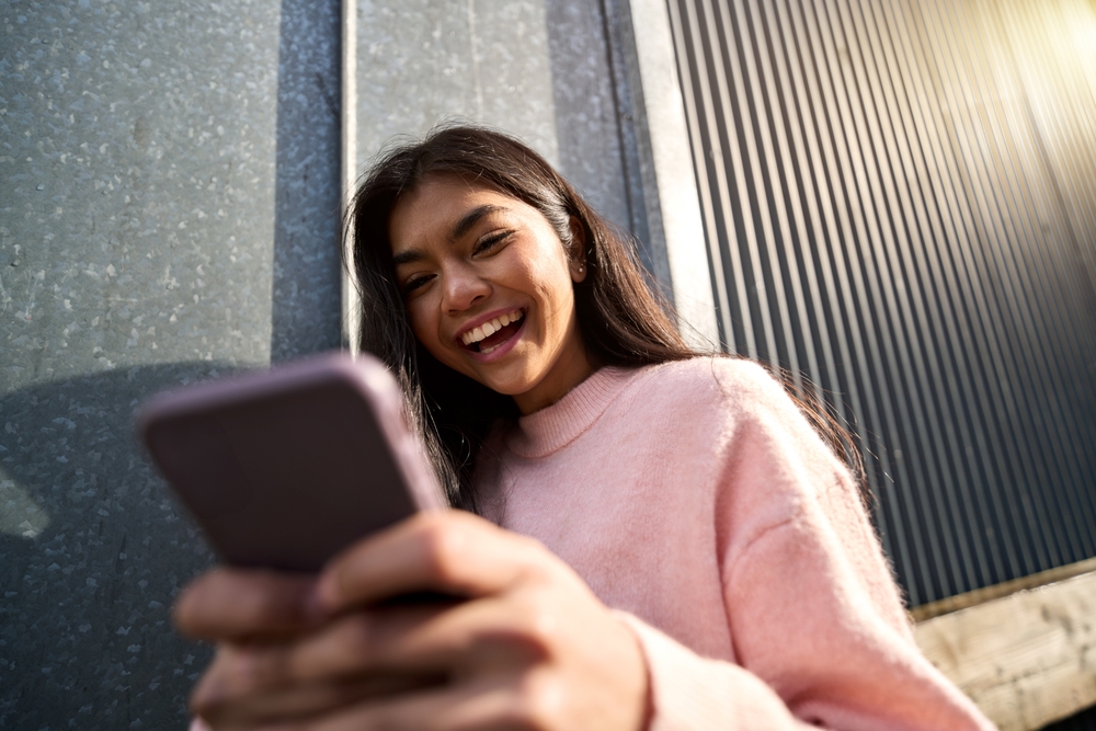 Smiling student using a smartphone outdoors, symbolizing digital engagement and social media strategies for how to market a school.