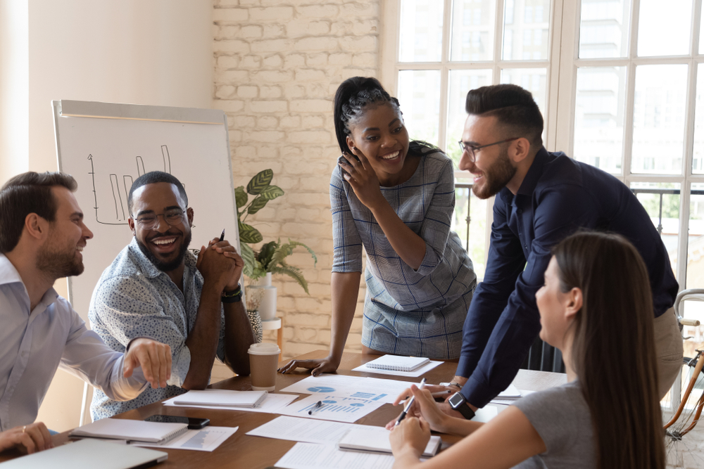 Diverse marketing team smiling and collaborating around a conference table with charts and a laptop, illustrating how AI in marketing enhances teamwork, creativity, and data-driven strategies.