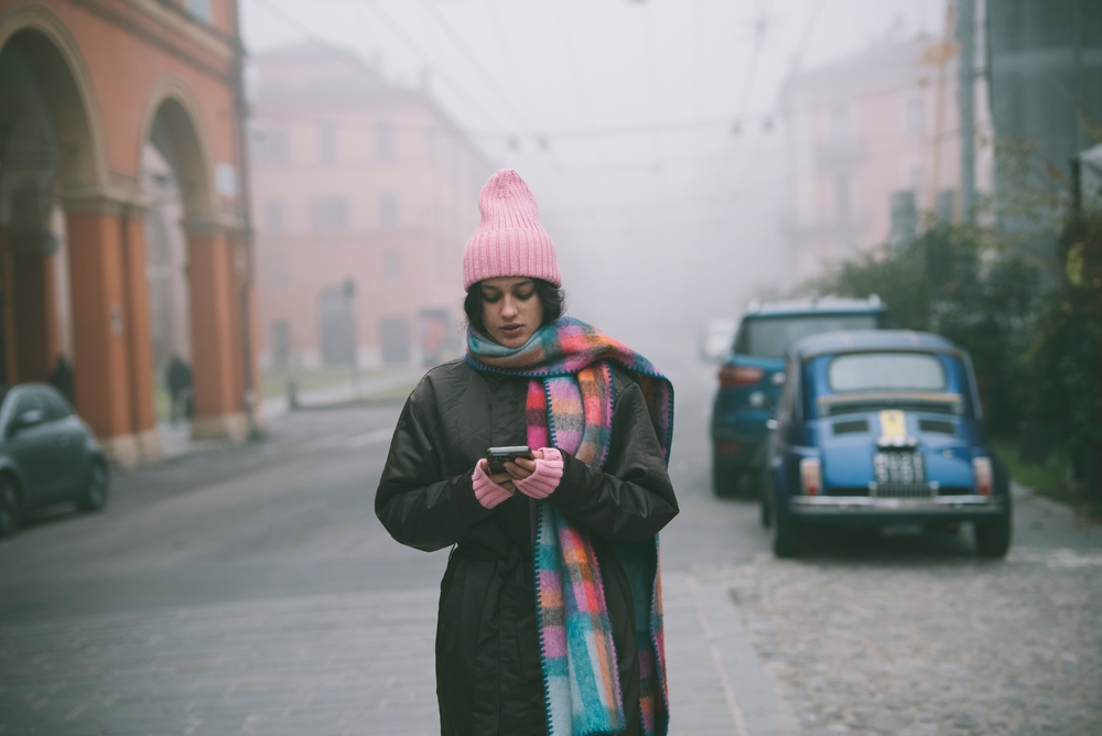 Woman walking on a foggy street checking her phone, illustrating search intent as users look for quick, on-the-go answers.