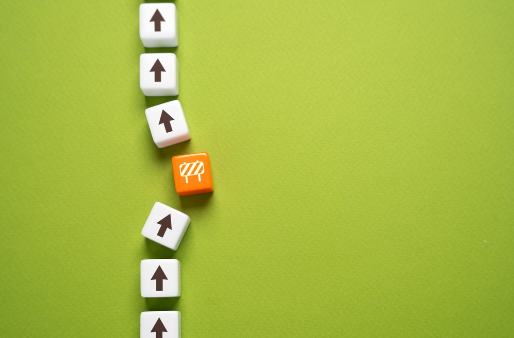 A row of white cubes with upward arrows is interrupted by a single orange cube displaying a barrier icon, visually representing what is a bottleneck in marketing and how obstacles can disrupt progress.