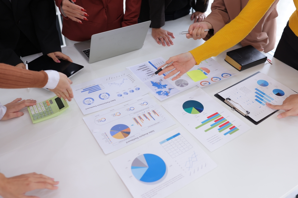 A team gathered around a table reviewing charts, graphs, and performance reports, illustrating how a fractional marketing agency analyzes data to guide strategy and improve business results.