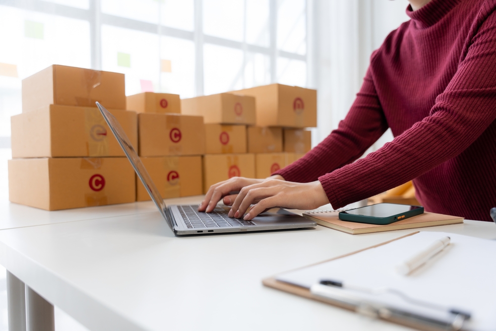 Small business owner working on a laptop with packaged orders on a desk, illustrating how to market an online business.