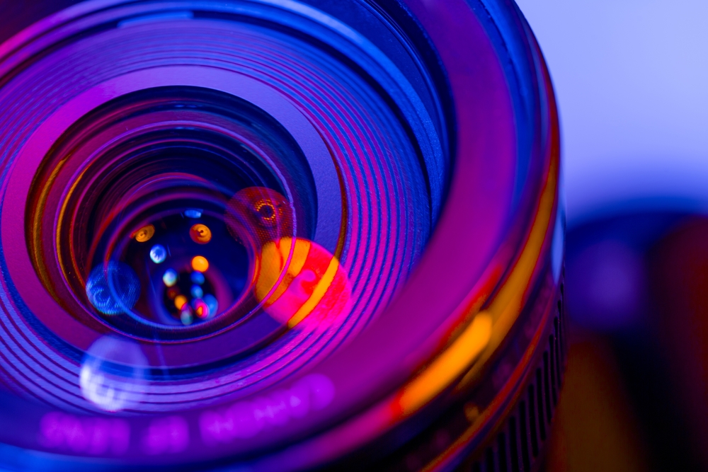 A close-up of a camera lens glowing with vibrant blue, purple, and orange lights, symbolizing creativity and precision in marketing video production.