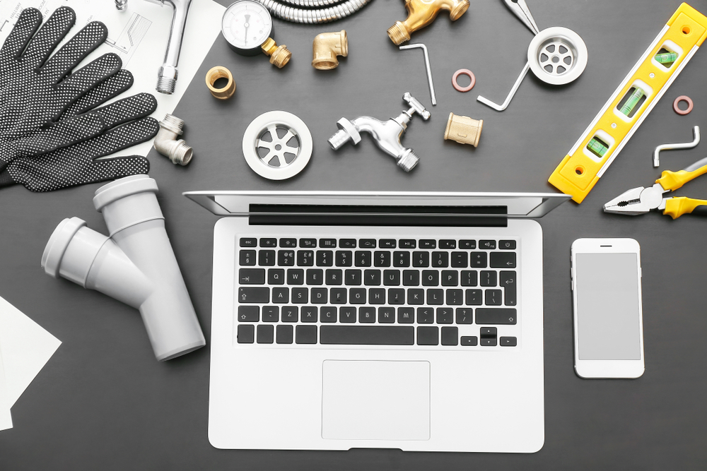 Laptop surrounded by plumbing tools and fittings, illustrating how to market a plumbing business by combining trade expertise with digital strategy.