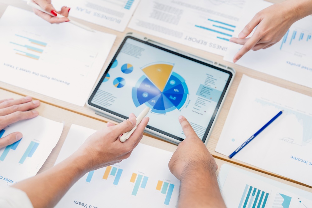 Business professionals analyze charts and performance data on a tablet, using collaborative insights to support strategic decision-making and thought leadership.