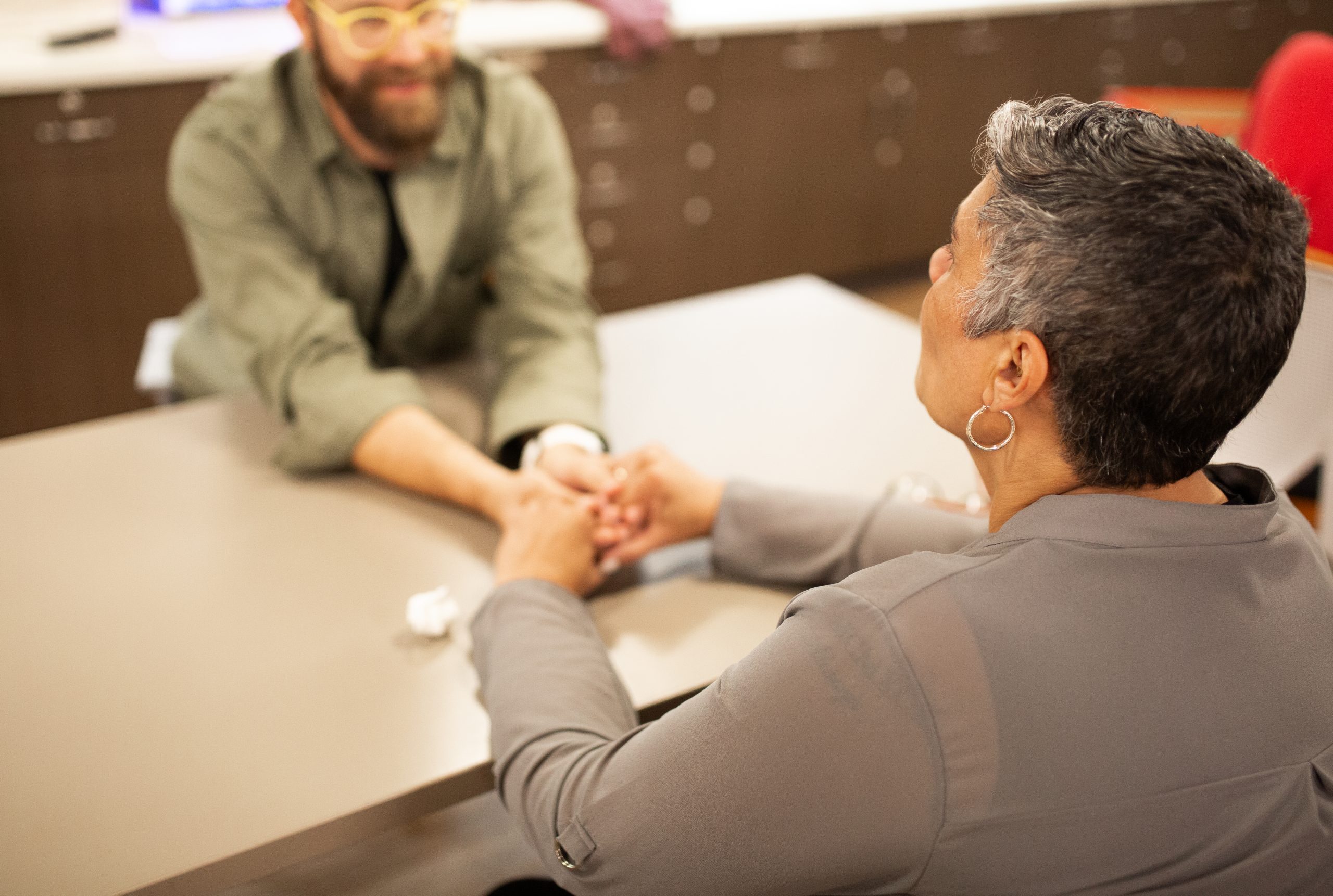 A filmmaker and an interview subject hold hands across a table during a documentary interview