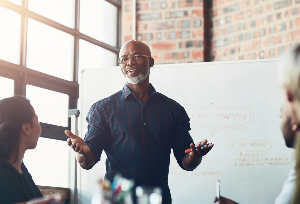 Business leader presenting ideas to colleagues in front of a strategy whiteboard, illustrating business storytelling in a collaborative workplace.