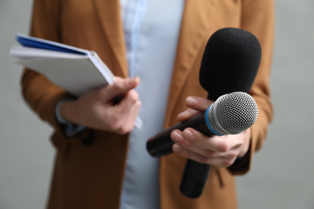 Journalist holding microphones and a notebook while reporting, illustrating How to Get Media Coverage for Your Business through press outreach and interviews.