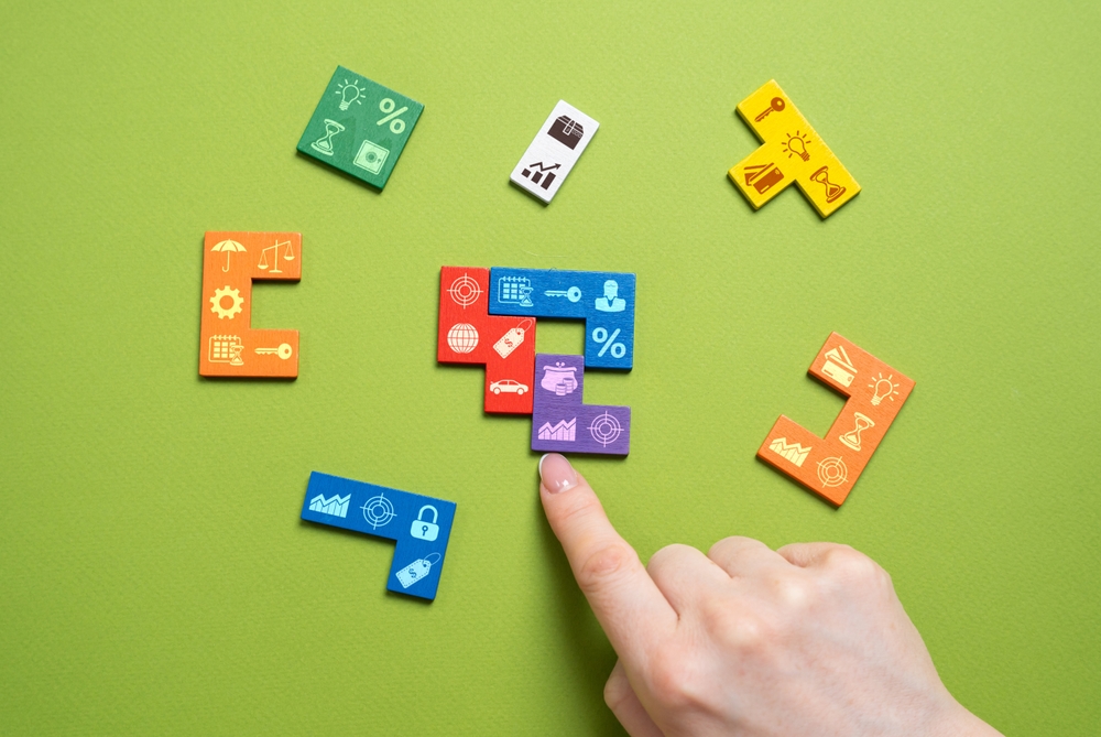 Hand arranging colorful puzzle pieces on a green background, illustrating demand generation best practices through strategy, targeting, planning, and optimization.