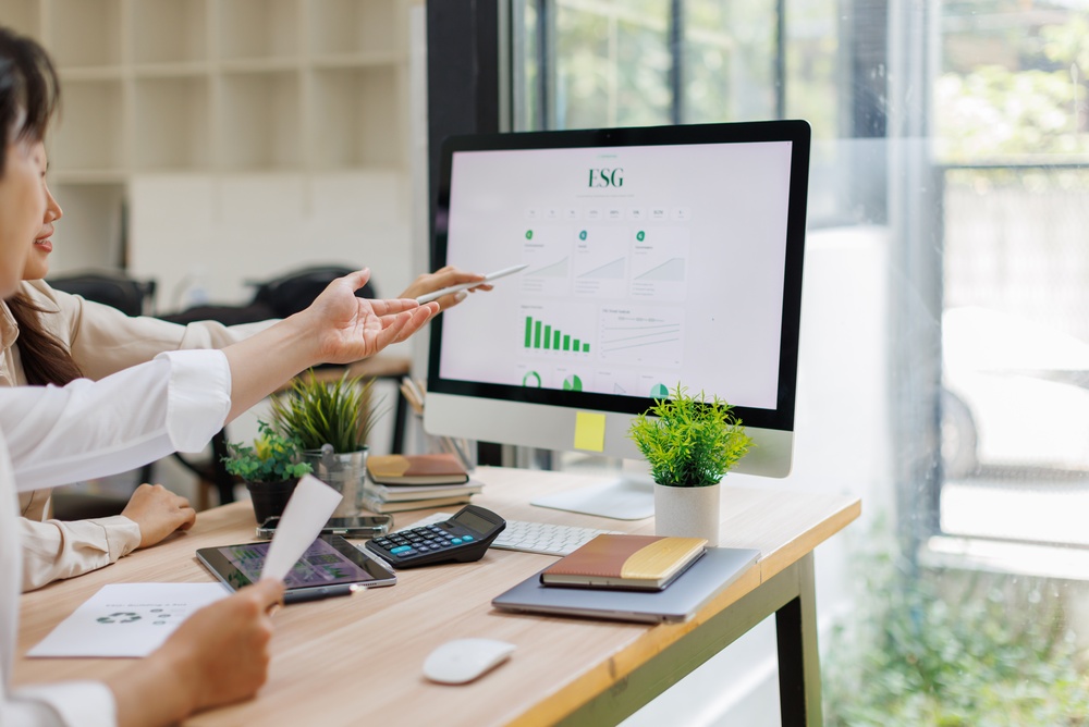 Two nonprofit professionals reviewing a nonprofit impact report with ESG metrics and performance data on a computer screen.