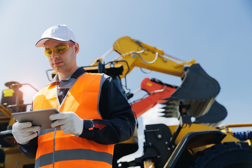 Construction professional using a tablet beside heavy equipment at a job site, illustrating construction marketing focused on project visibility, technology, and business growth.