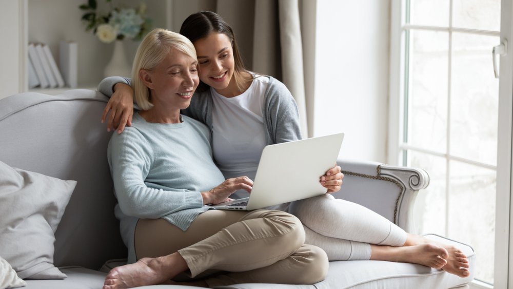 Grown daughter and her mother sharing a laptop on the sofa, researching care options the way assisted living advertising reaches families.