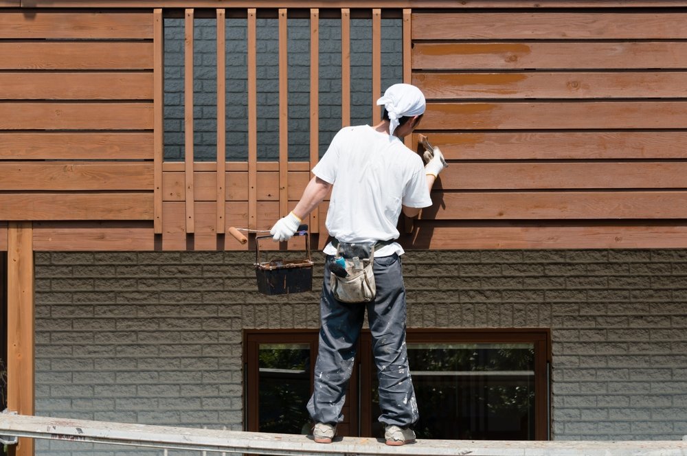 Painter applying stain to a house exterior wall, one of the home improvement advertising ideas that show proof of work