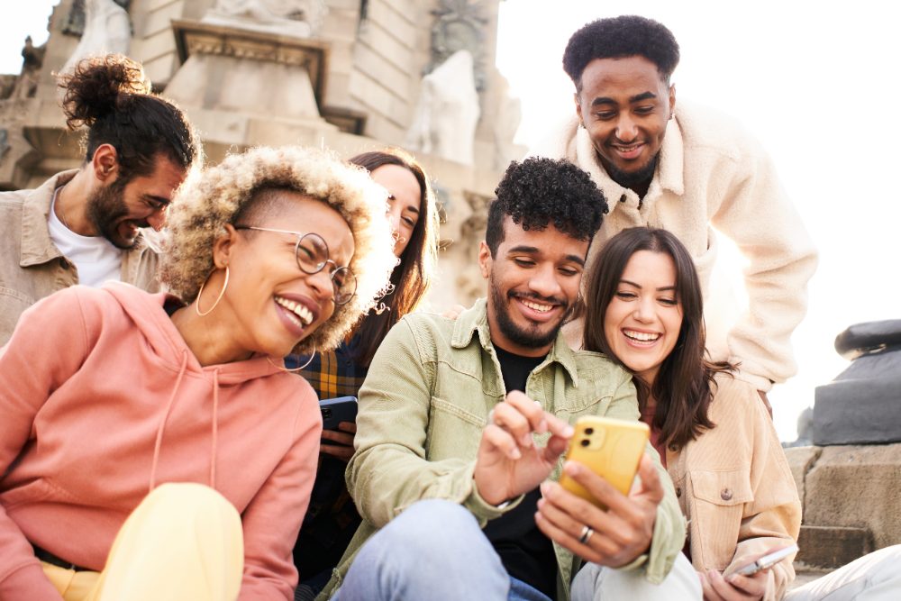 Group of friends laughing as they watch a short video on a phone, the audience a video content strategy has to reach.