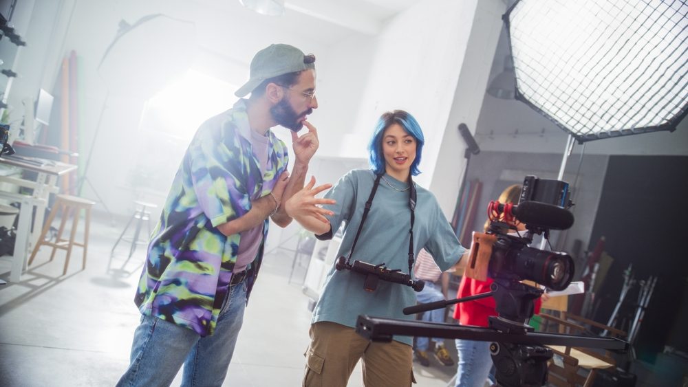 Two filmmakers discussing a shot beside a camera rig on set, planning one filming block for a video marketing strategy.