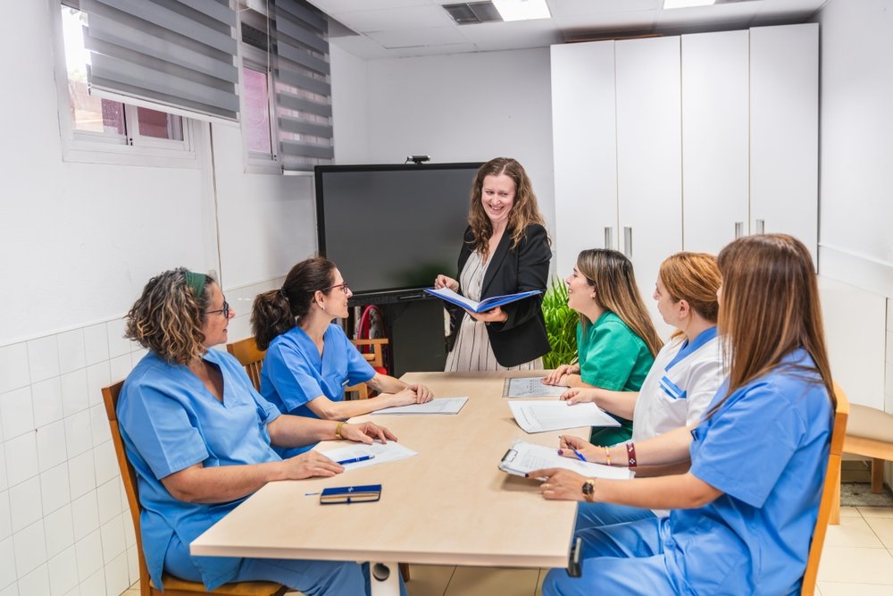 Care coordinator holding a folder while nurses around a table review notes together, mapping out an assisted living marketing plan.